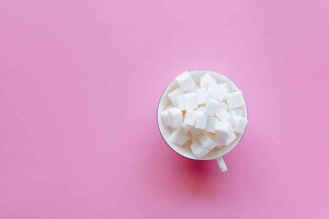 pexels-photo-6940868-6940868 Top view of a cup filled with sugar cubes on a vibrant pink background.